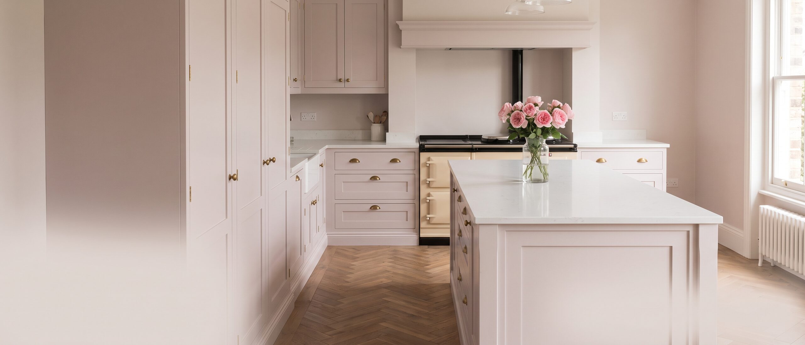 A pale blush-grey handcrafted shaker kitchen with a white quartz island and garden roses